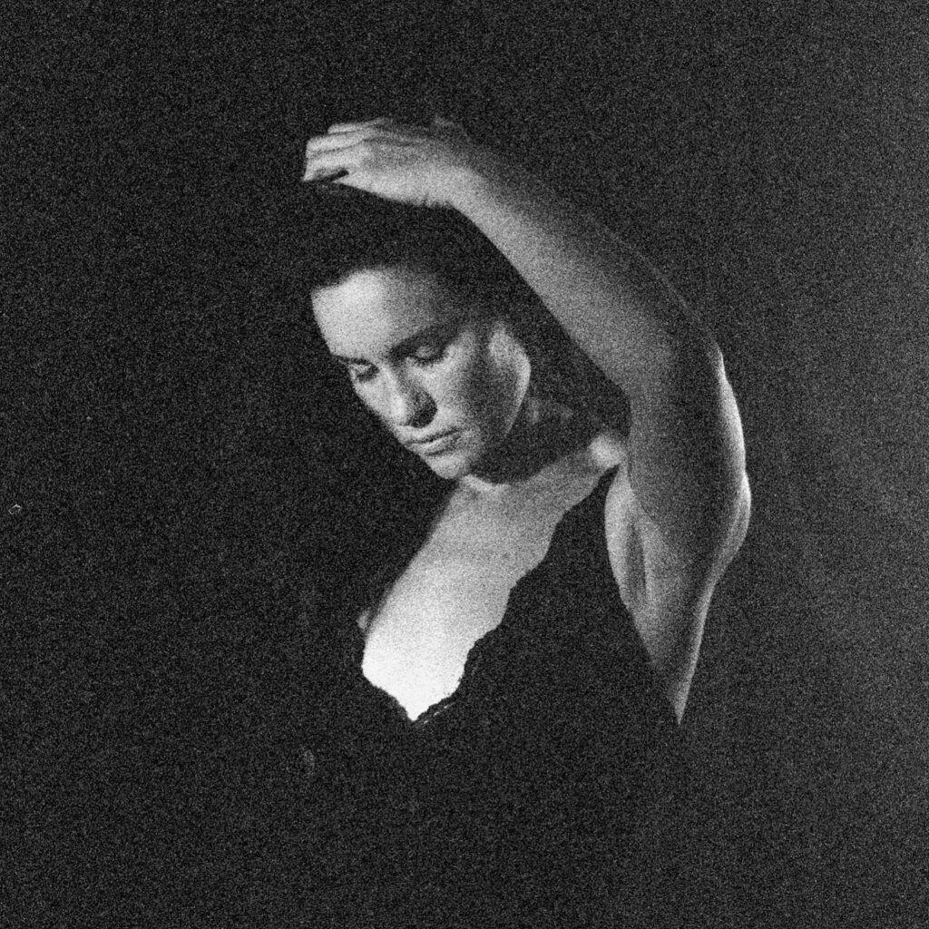 Black and white image of woman in the dark touching her hair.