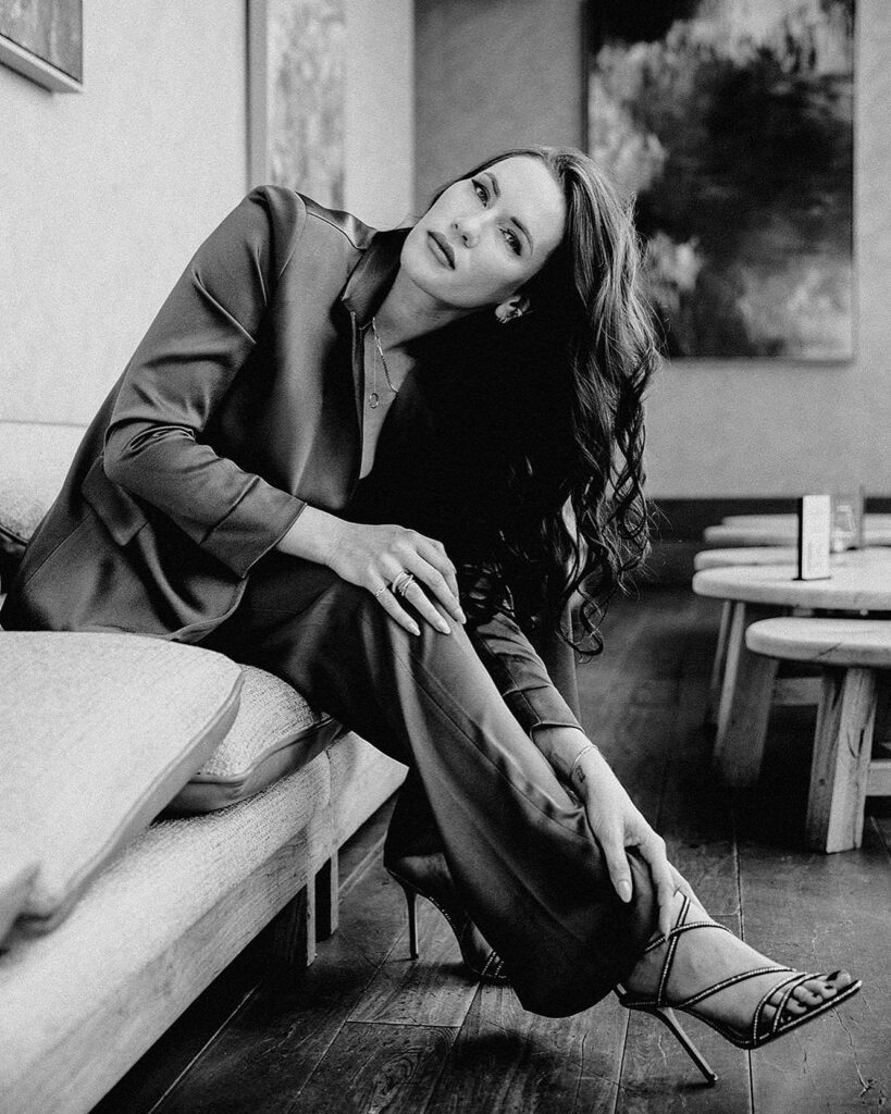 Black and white image of woman on a couch, in a suit, touching her hair. 