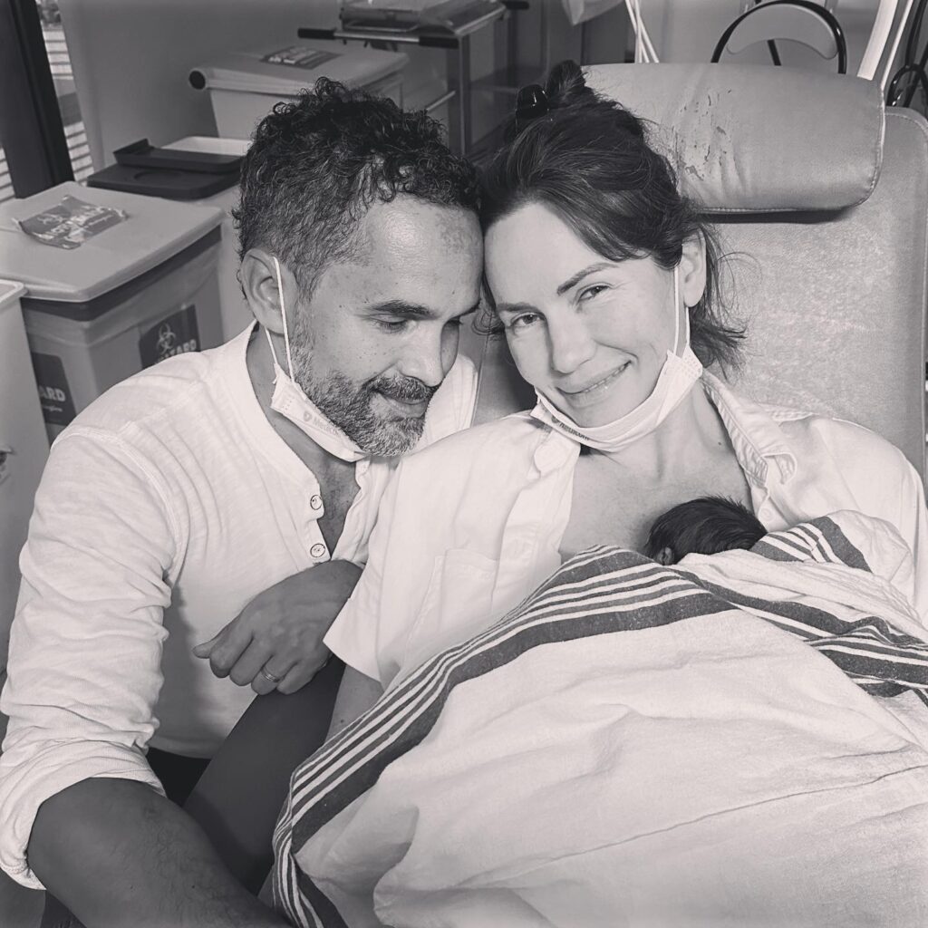 Image of couple holding their newbord baby and smiling.