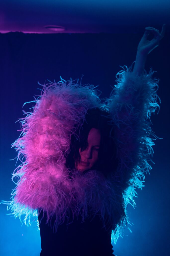 Image of woman in a feather jacket, arms up in the air